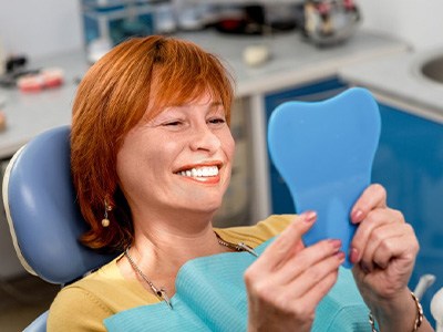 Woman smiling in the patient’s chair while looking in a mirror
